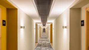 A hotel hallway with a patterned carpet, numbered doors, and wall-mounted lights. - Zentral Ave (Zaragoza)