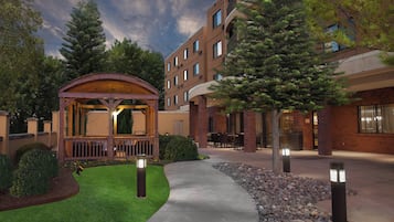 Un patio de hotel con un quiosco de madera, mobiliario exterior y un césped bien cuidado.