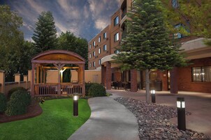 Un patio de hotel con un quiosco de madera, mobiliario exterior y un césped bien cuidado.