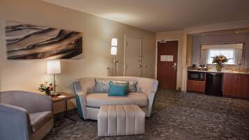 A hotel room with a sofa, ottoman, lamp, and a painting on the wall.