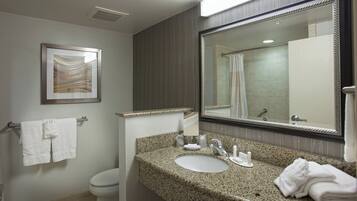A bathroom with a granite countertop sink, a large mirror, a framed artwork above the sink, a towel rack with towels, and a toilet.