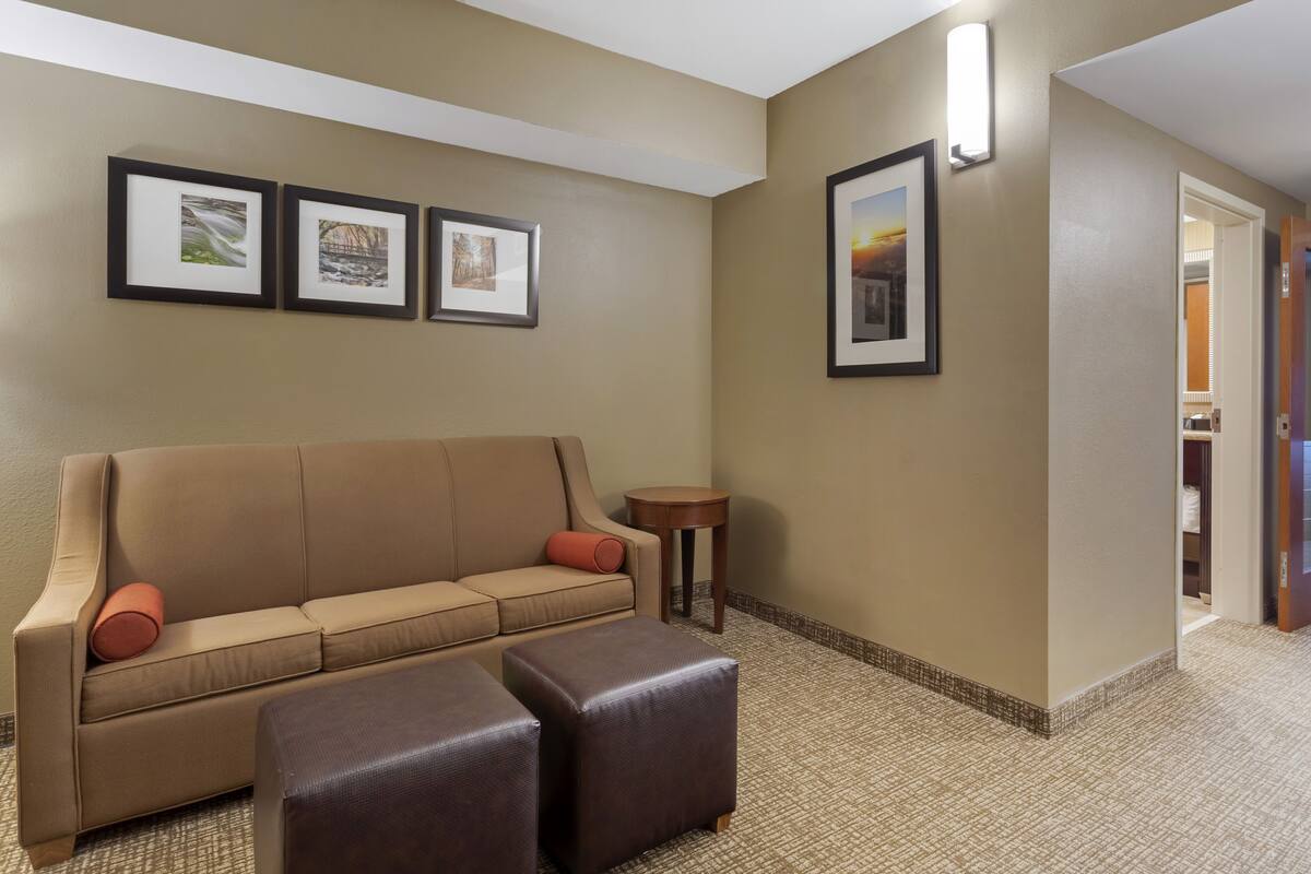 A hotel lobby with a beige sofa, two ottomans, framed pictures on the wall, and a small round table.