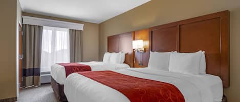 A hotel room with two beds, a large window with curtains, a wall-mounted lamp, and a red throw blanket.