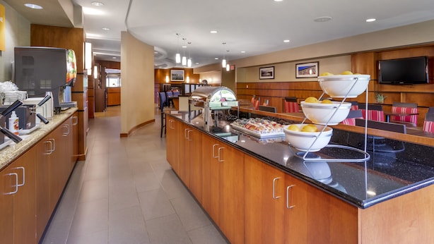 Un'area colazione in hotel con un buffet, inclusa una postazione caffè, un'esposizione di frutta e posti a sedere.