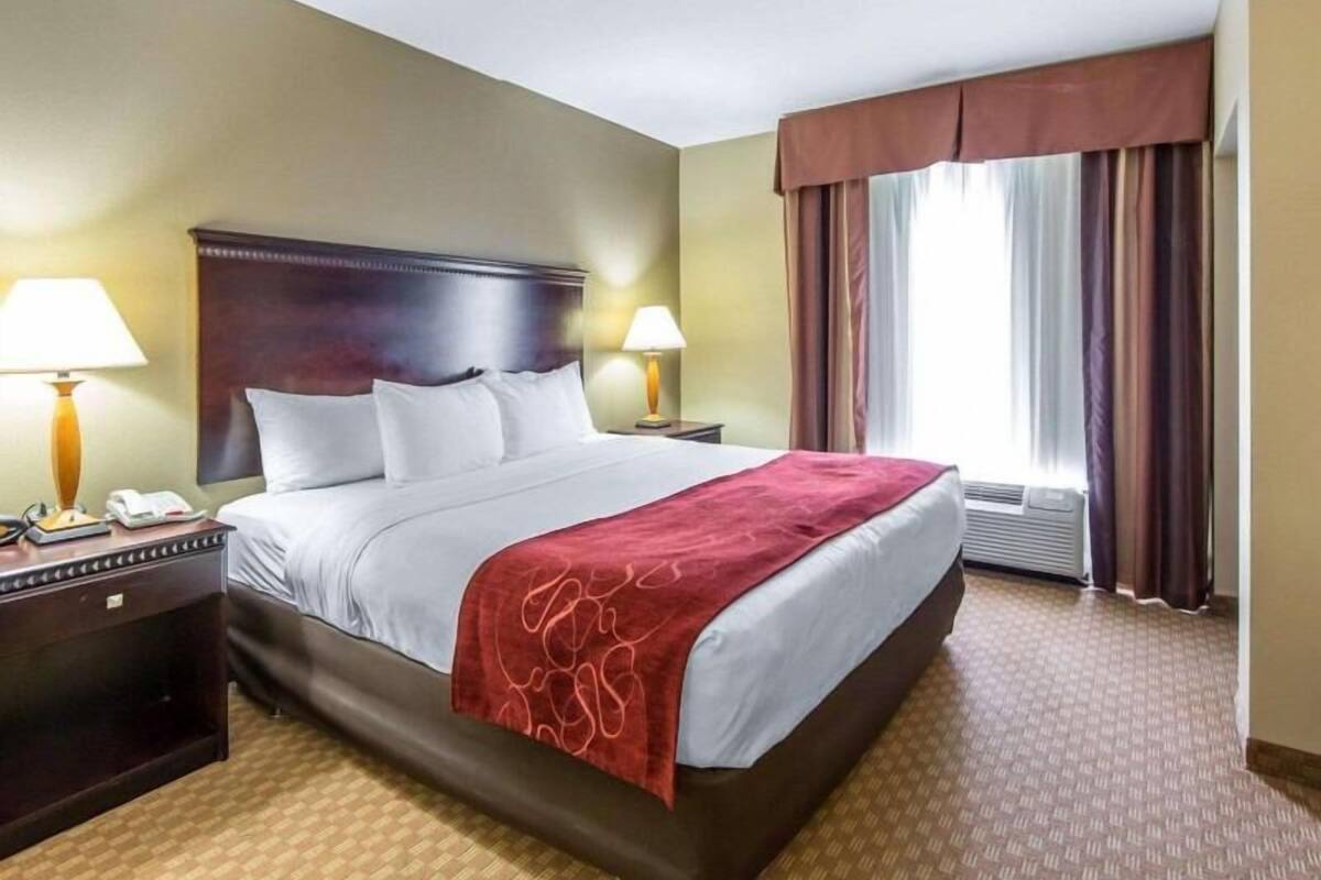 A hotel room with a large bed, two bedside lamps, a telephone, and a window with curtains.