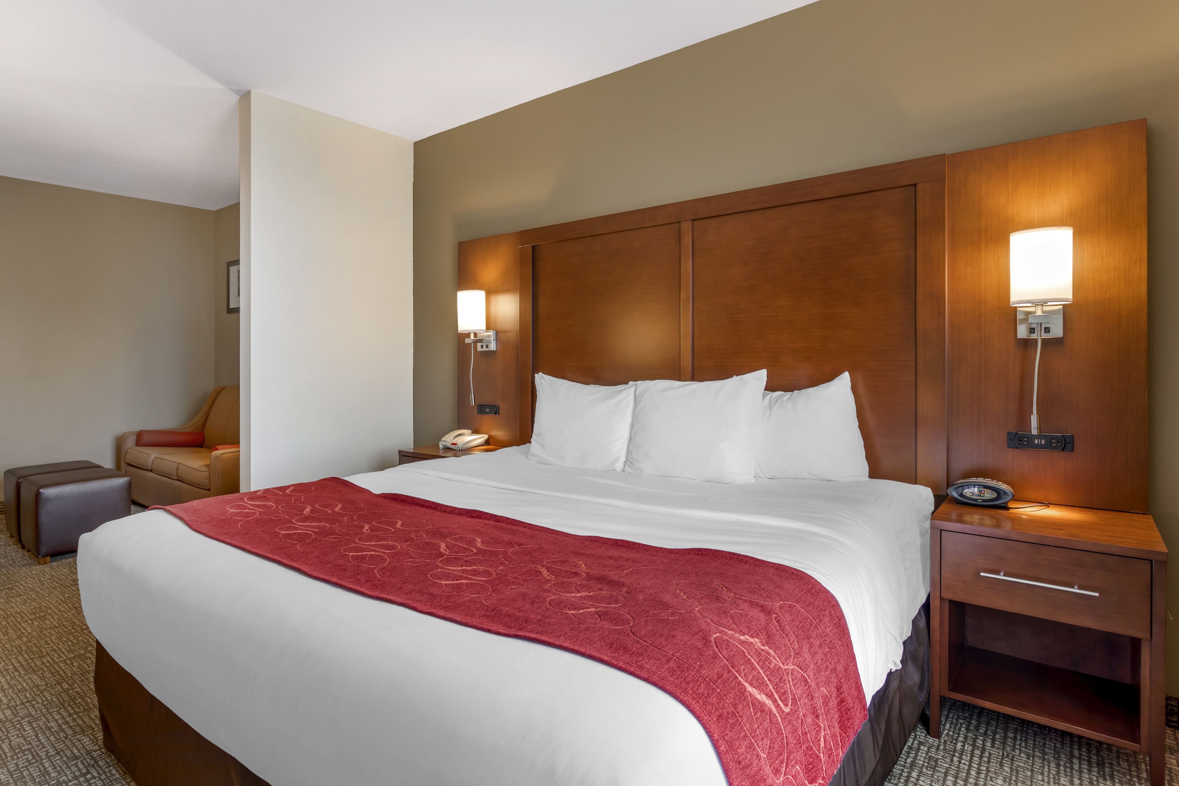 A hotel room with a large bed, a wooden headboard, bedside lamps, a nightstand, a chair, and a small table.