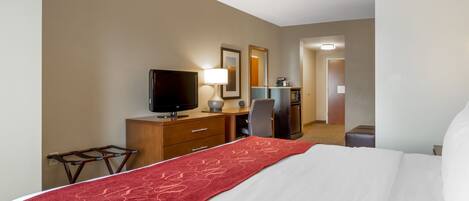 A hotel room with a bed, a desk with a computer, a television, and a mirror.