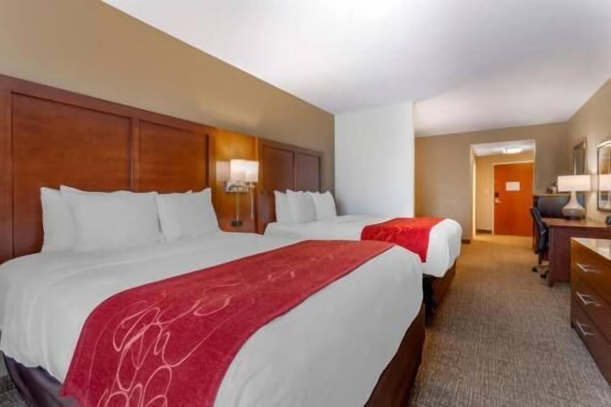 A hotel room with two beds, a desk, and a door.