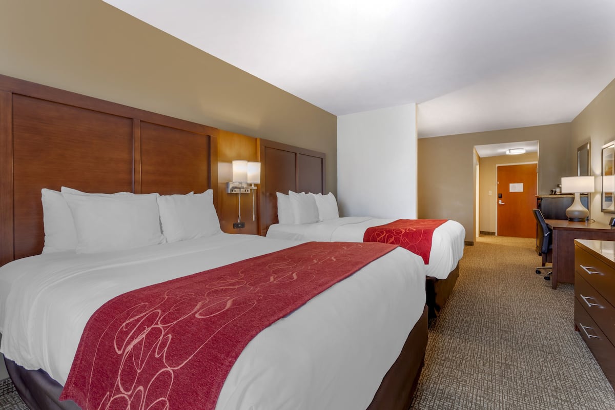 A hotel room with two beds, a desk, and a chair.