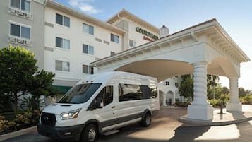 A white van parked under a white canopy with the text "COURTYARD" on it, in front of a hotel building with multiple windows and balconies.