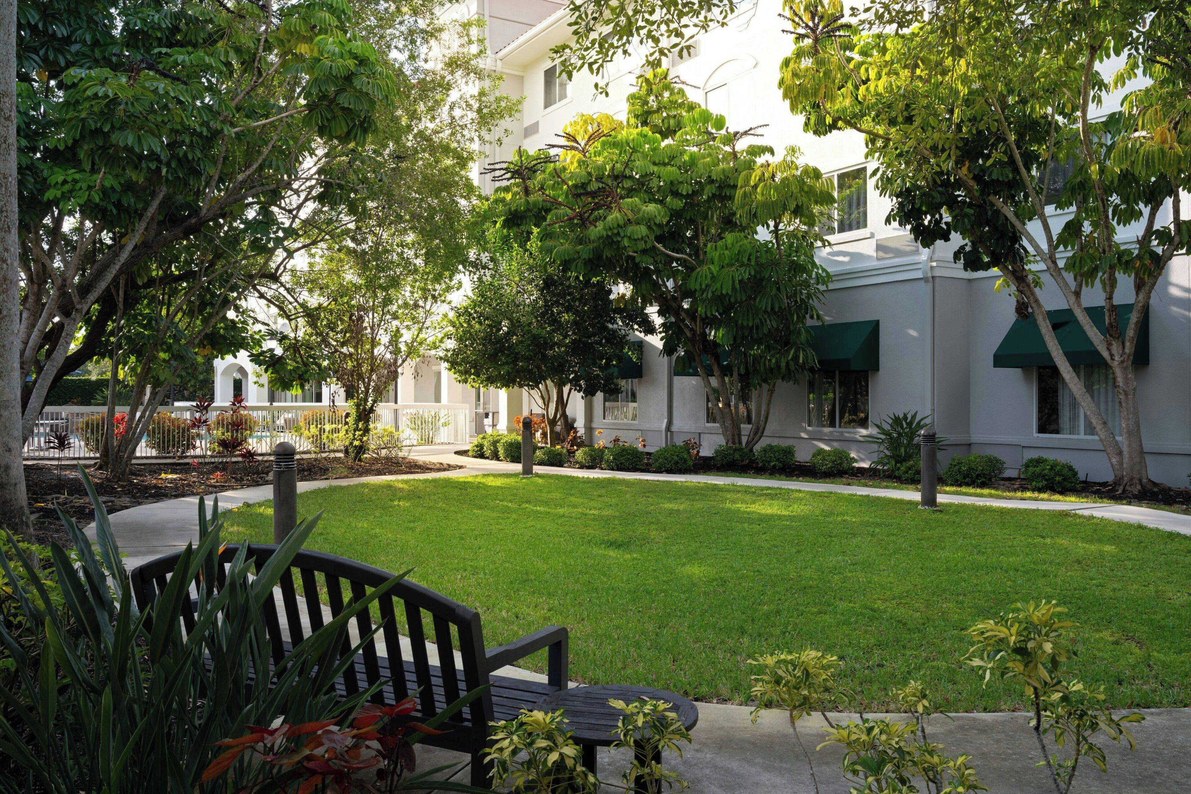Un patio con un banco, rodeado de árboles y un edificio con toldos verdes.