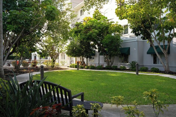A courtyard with a bench, surrounded by trees and a building with green awnings.