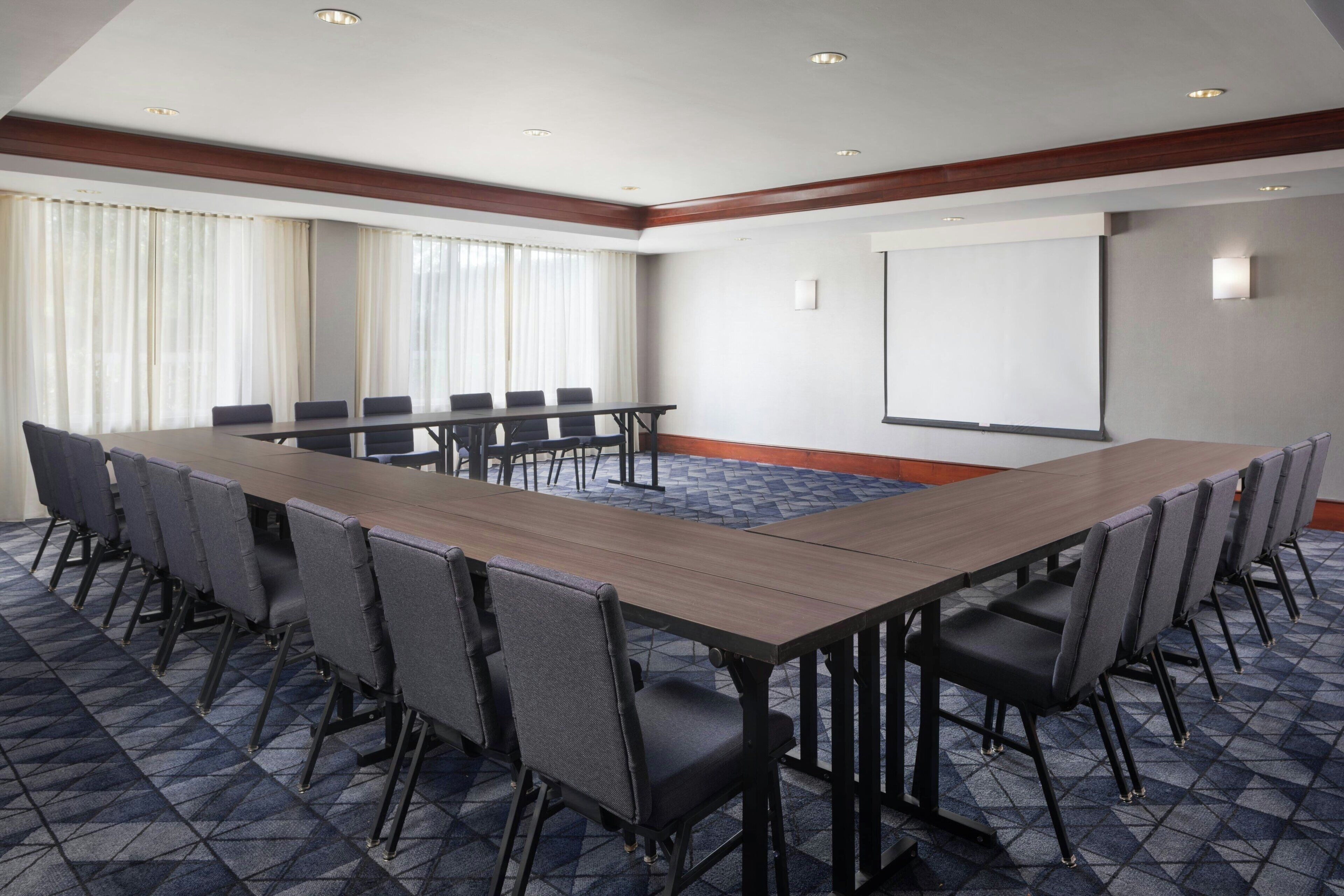 Une salle de conférence avec une longue table, de nombreuses chaises, un écran de projection et un sol recouvert de moquette.