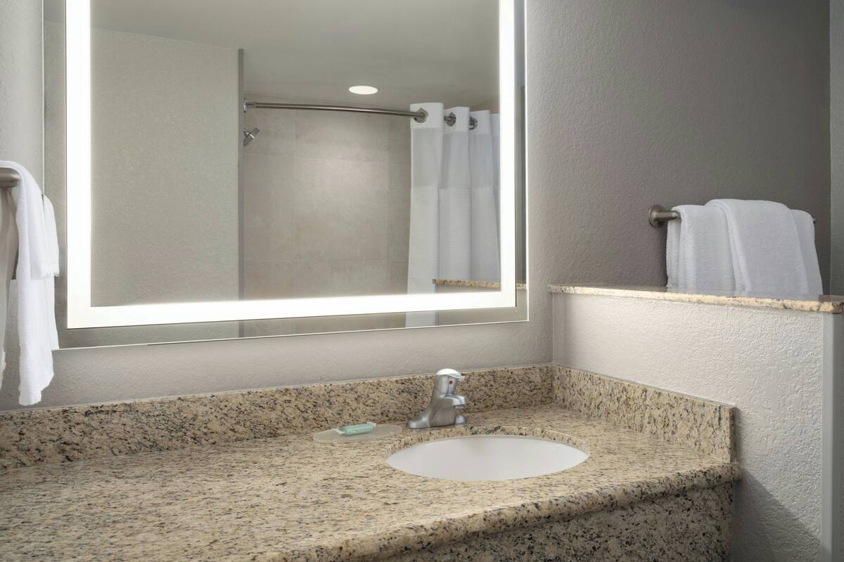 A bathroom with a granite countertop, a sink, a mirror, and a shower area.