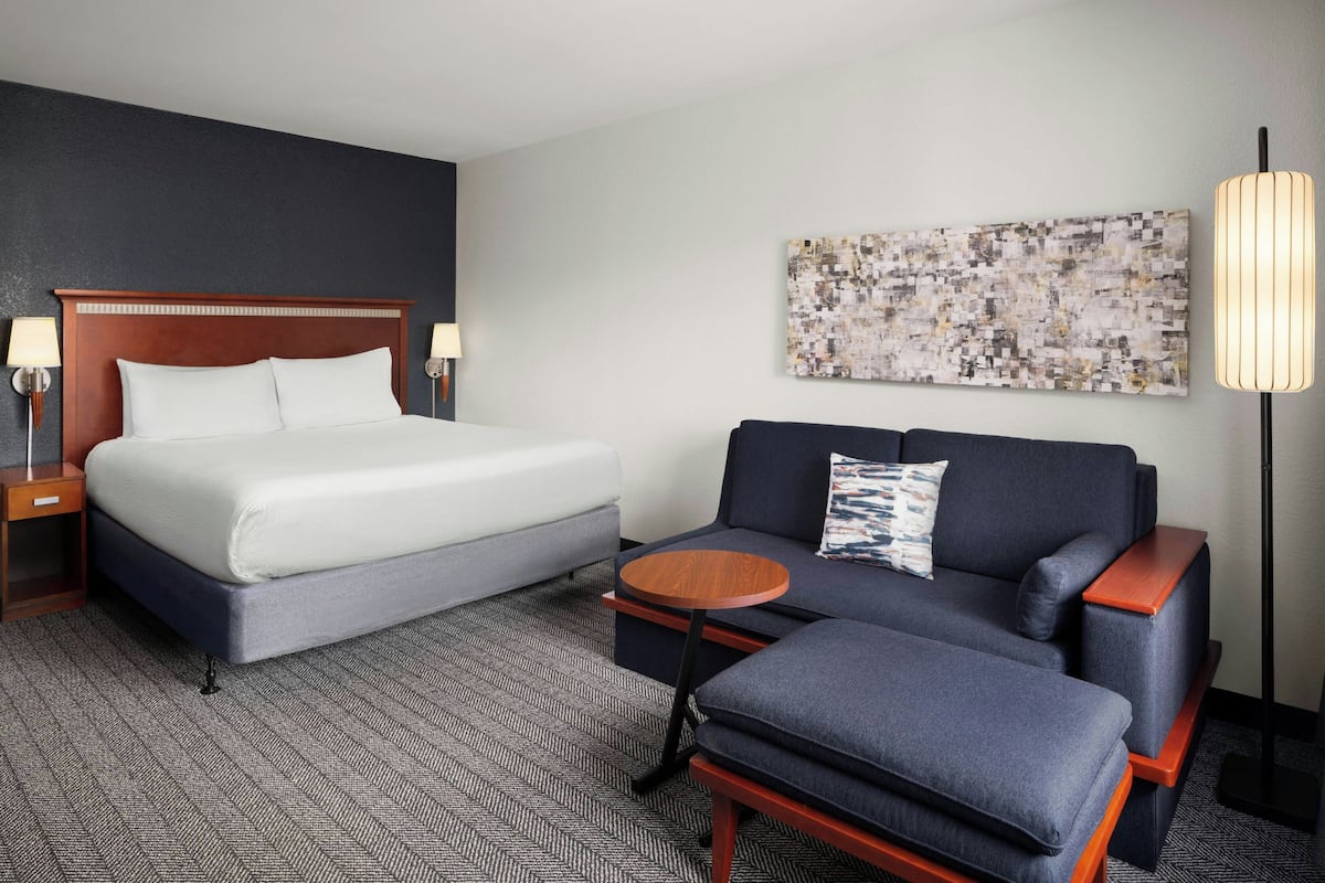 A hotel room with a bed, a sofa, a small table, and a floor lamp.