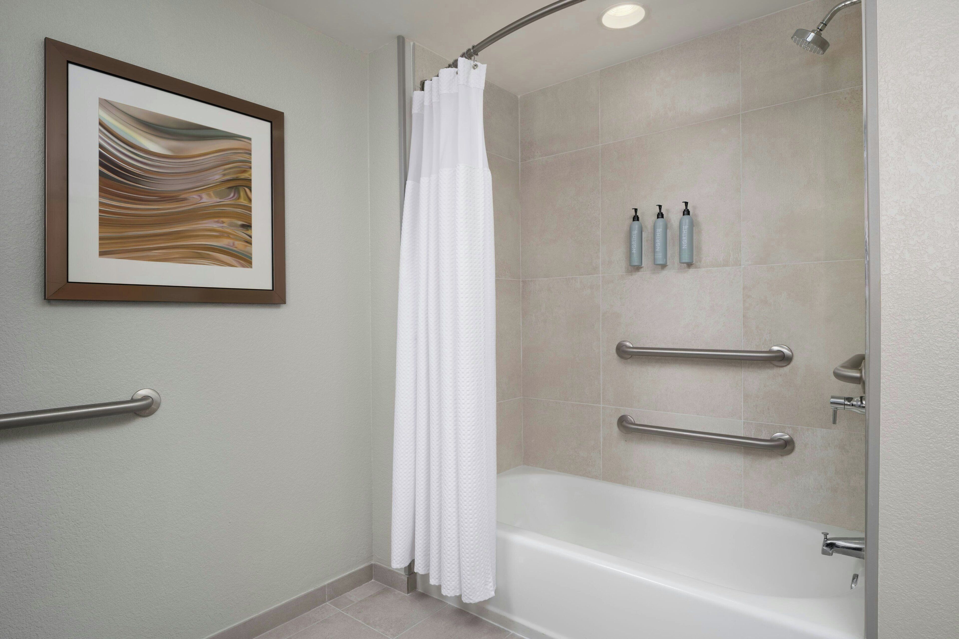 A modern bathroom with a bathtub, shower, and handrails.