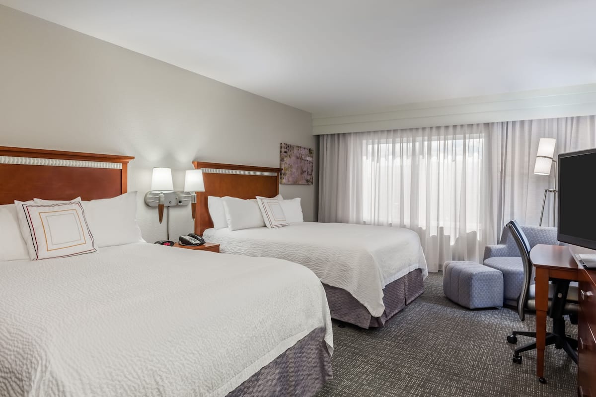 A hotel room with two beds, a desk, a chair, a TV, and a window with curtains.