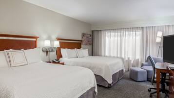 A hotel room with two beds, a desk, a chair, a TV, and a window with curtains.