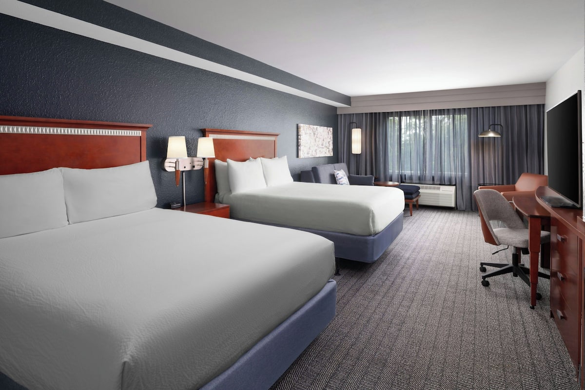 A hotel room with two beds, a desk, a chair, a TV, and a window with curtains.