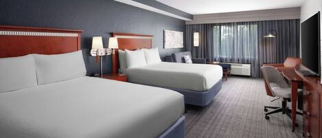 A hotel room with two beds, a desk, a chair, a TV, and a window with curtains.
