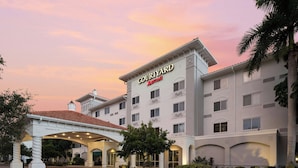 Un hotel Courtyard Marriott con entrada cubierta, varios pisos y cielo despejado.