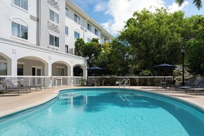 A swimming pool area with lounge chairs and umbrellas, surrounded by a building with balconies and a white facade. - Courtyard by Marriott Fort Myers I-75/Gulf Coast Town Center (Fort Myers)
