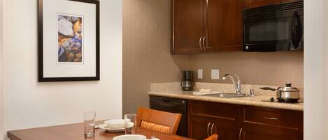 A kitchen with wooden cabinets, a microwave, a coffee maker, and a dining table with chairs.