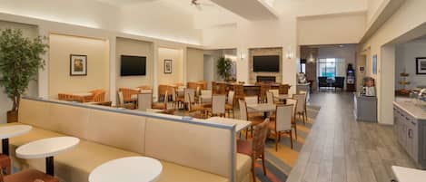 Un moderno vestíbulo de hotel con zona de estar, mesas de comedor, chimenea y área de cocina.