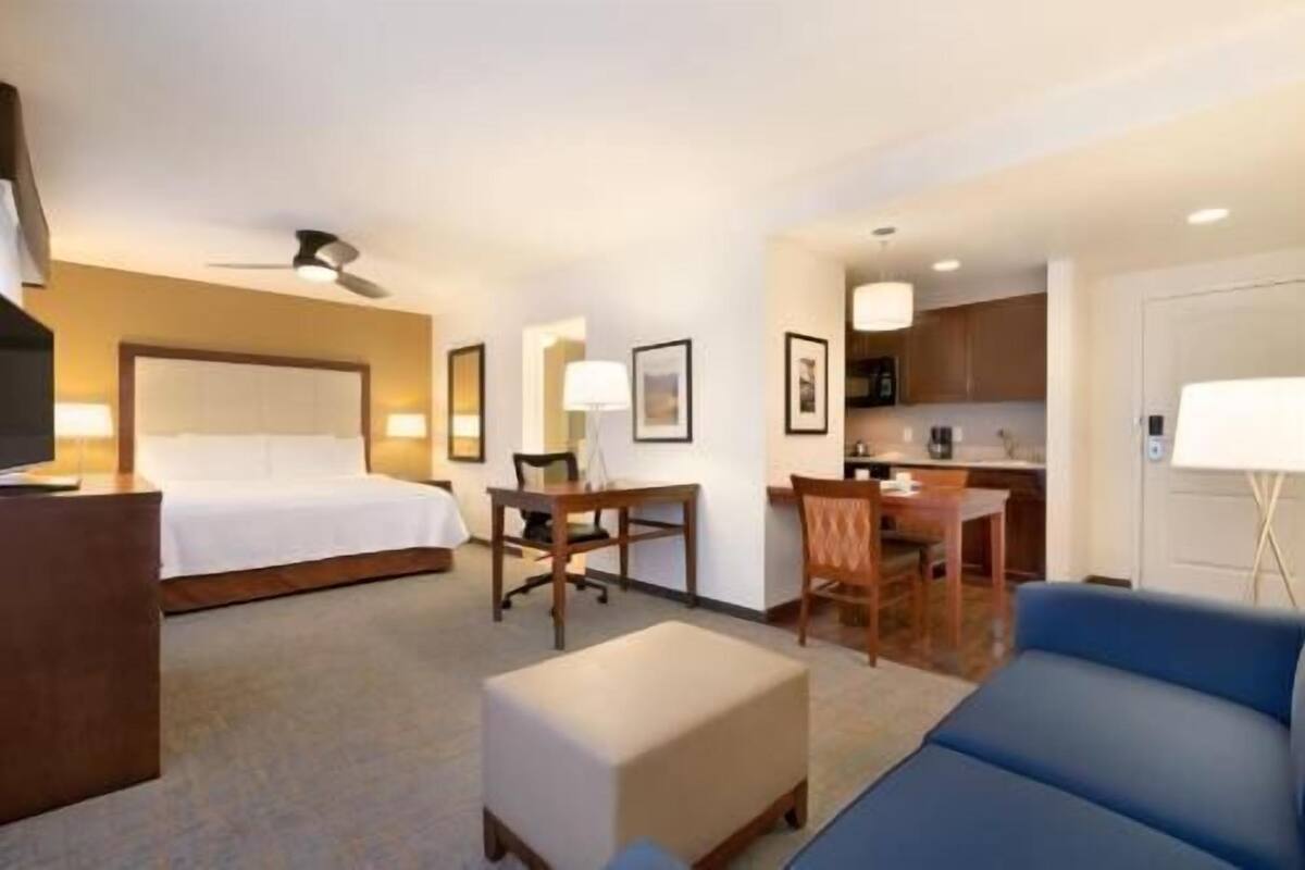 Ein Hotelzimmer mit Bett, Schreibtisch, Stuhl, Hocker und einem blauen Sofa.