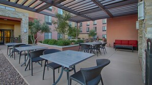 Un patio al aire libre con mesas y sillas, un sofá rojo y un muro de piedra.