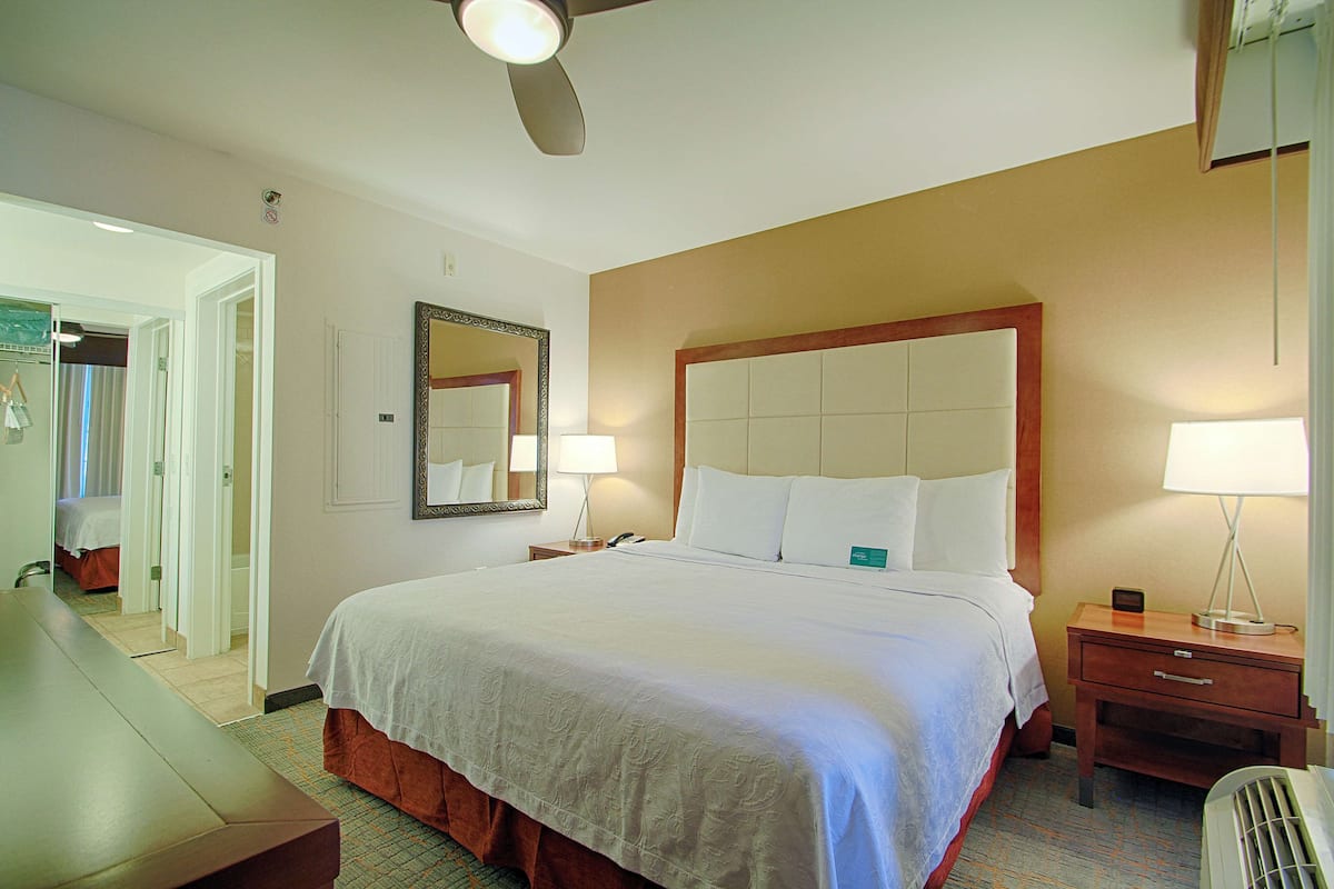 Ein Hotelzimmer mit einem großen Bett, Nachttischen, einem Schreibtisch und einem Deckenventilator.