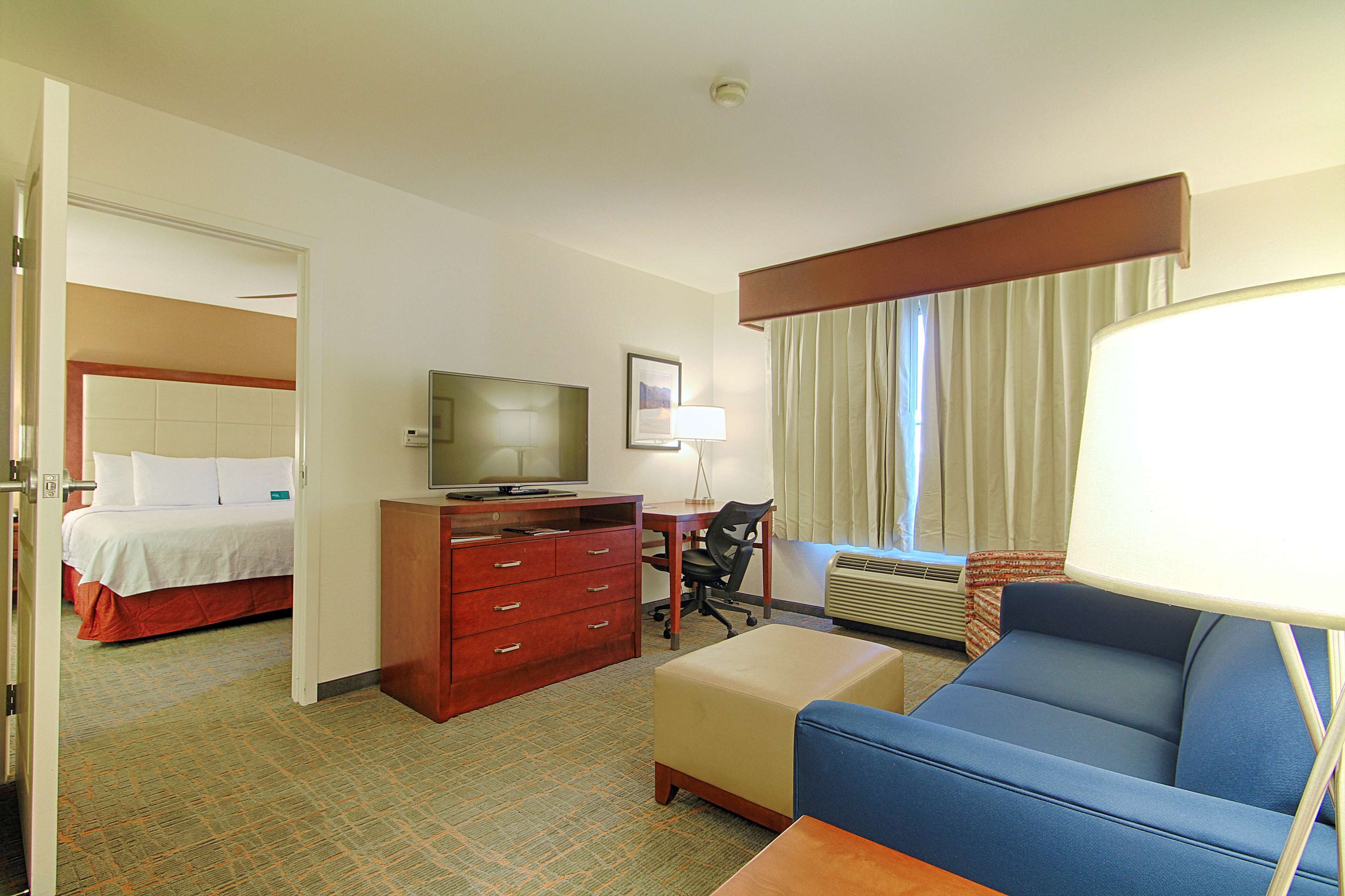 A hotel room with a bed, a desk with a television, a chair, a sofa, and a lamp.