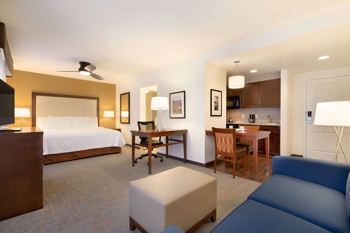Ein Hotelzimmer mit Bett, Schreibtisch, Stuhl, Sofa, kleinem Tisch und einer Küchenzeile.