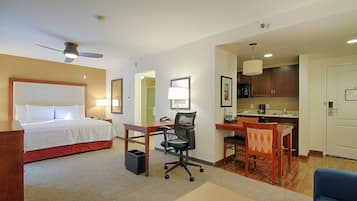 Ein Hotelzimmer mit Bett, Schreibtisch, Stuhl, Küchenzeile und Deckenventilator.