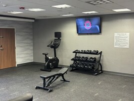 Un gimnasio con equipo de ejercicio, una pantalla de televisión y un cartel con las normas de uso.