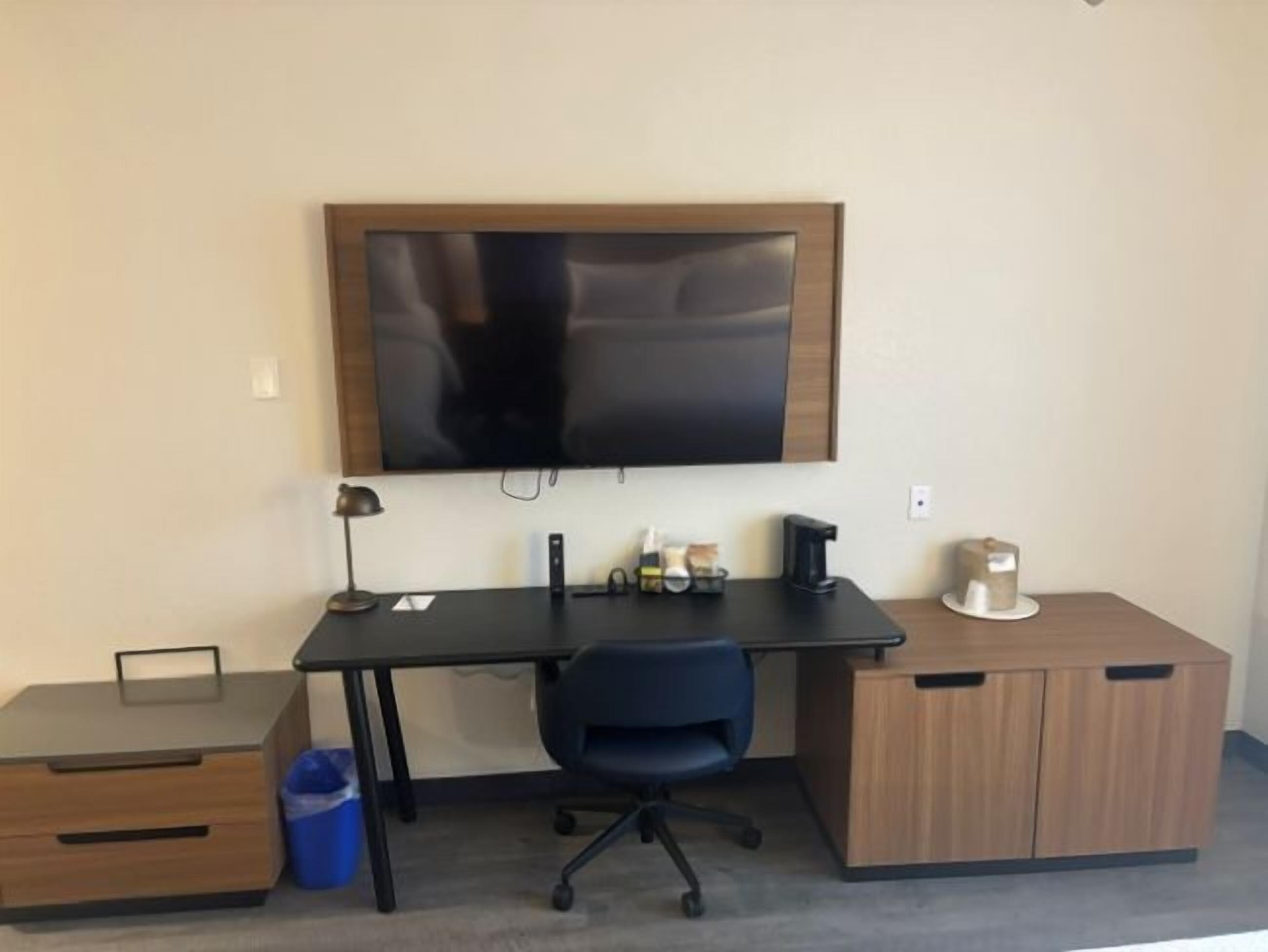 A room with a desk, chair, TV, and storage cabinets.