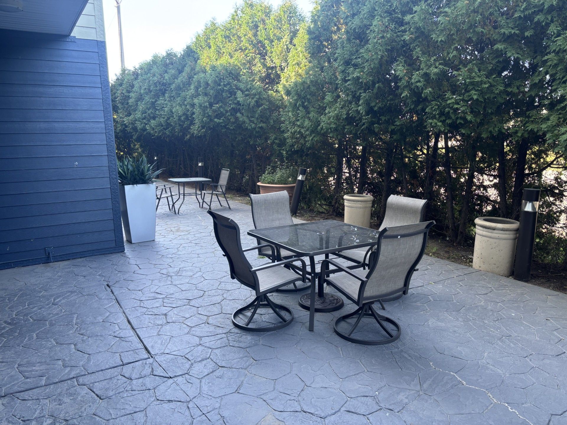 Un patio con una mesa y sillas, rodeado por un seto y un edificio.
