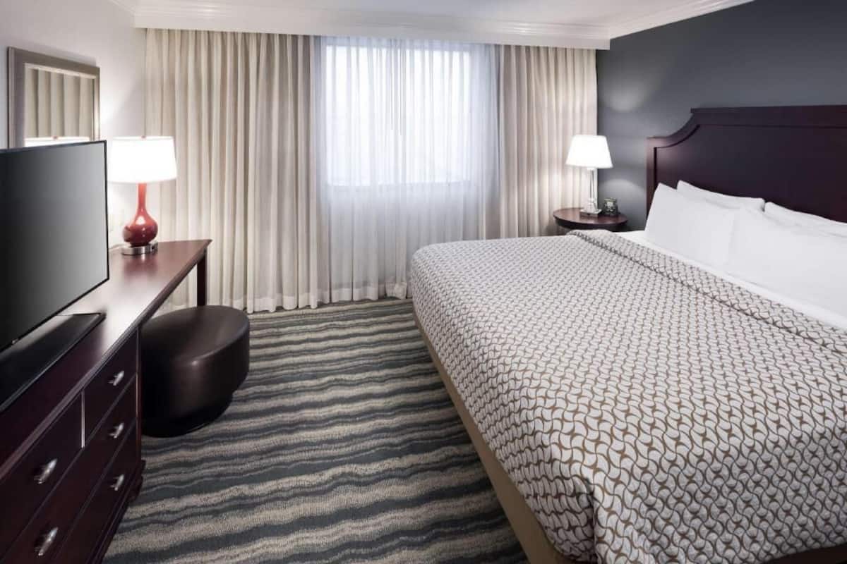 Une chambre d’hôtel comprenant un lit, une télévision, un bureau, une chaise, une table de chevet et une fenêtre avec des rideaux.