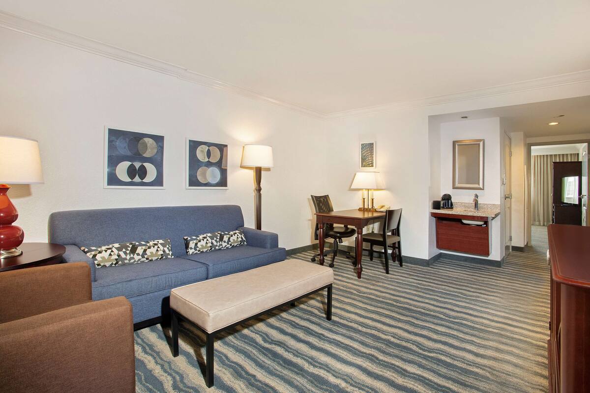 Une chambre d’hôtel avec un canapé bleu, une petite table, un banc et un coin repas comprenant des chaises et une table.