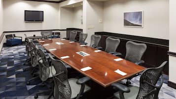 A conference room with a long table, multiple chairs, a flat-screen TV, and a painting on the wall.