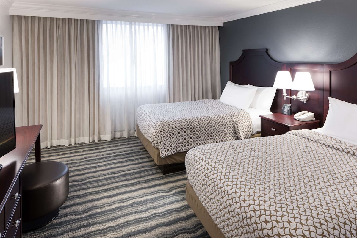 Une chambre d’hôtel avec deux lits, un bureau, une chaise, une lampe et un téléphone sur la table de chevet.