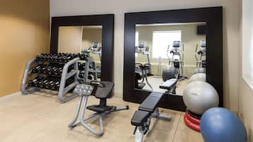 Une salle de sport équipée de matériel d’exercice, d’un banc, d’haltères et de ballons d’exercice.