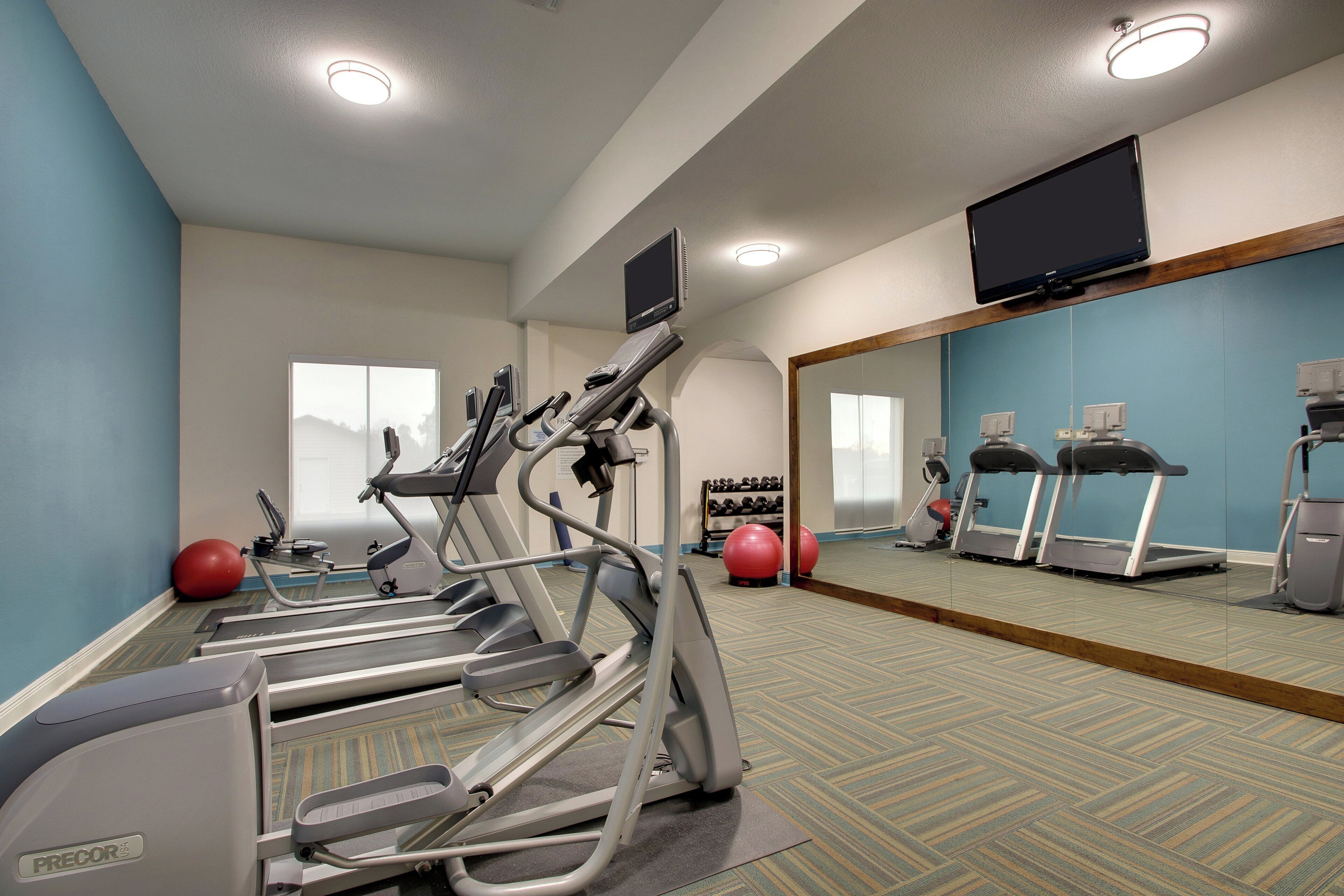 Un gimnasio con cintas de correr, pelotas de ejercicio y un espejo grande.
