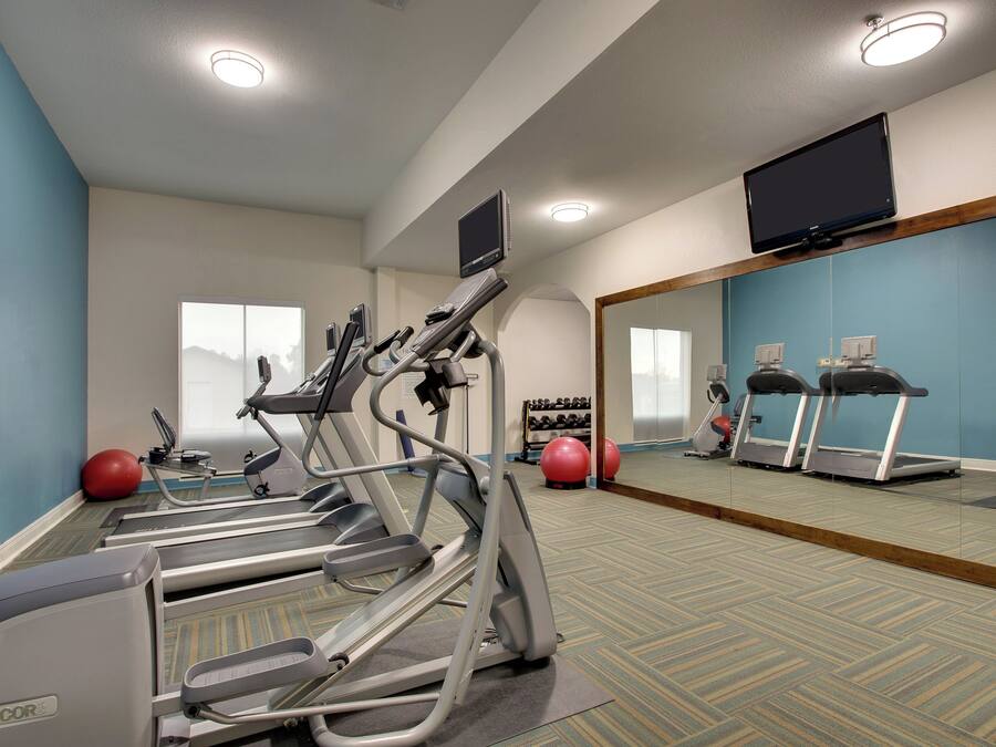 Un gimnasio con cintas de correr, pelotas de ejercicio y un espejo grande.