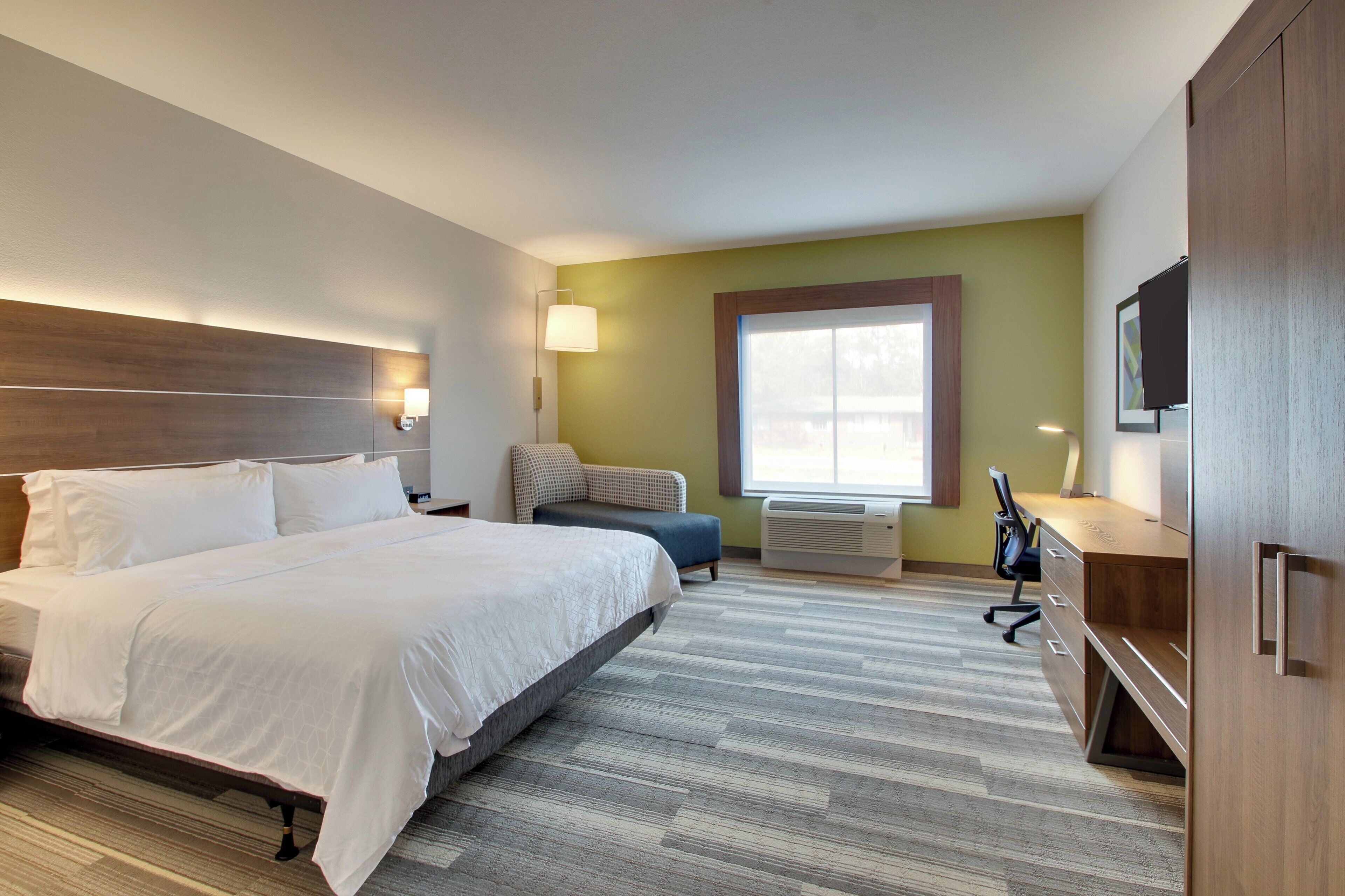 A hotel room with a large bed, a desk, a chair, a TV, and a window.