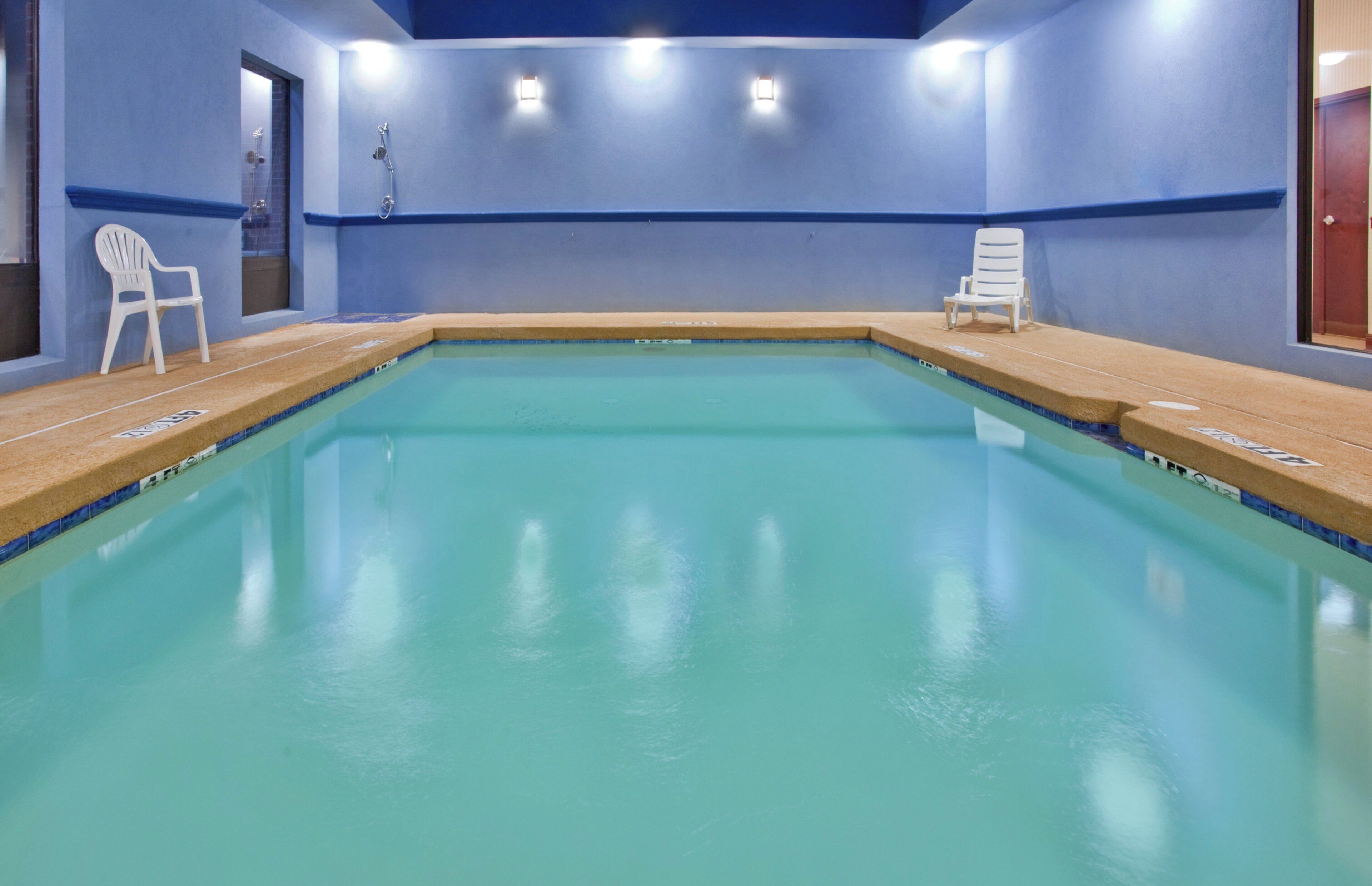 Une piscine avec deux chaises blanches et un espace douche.