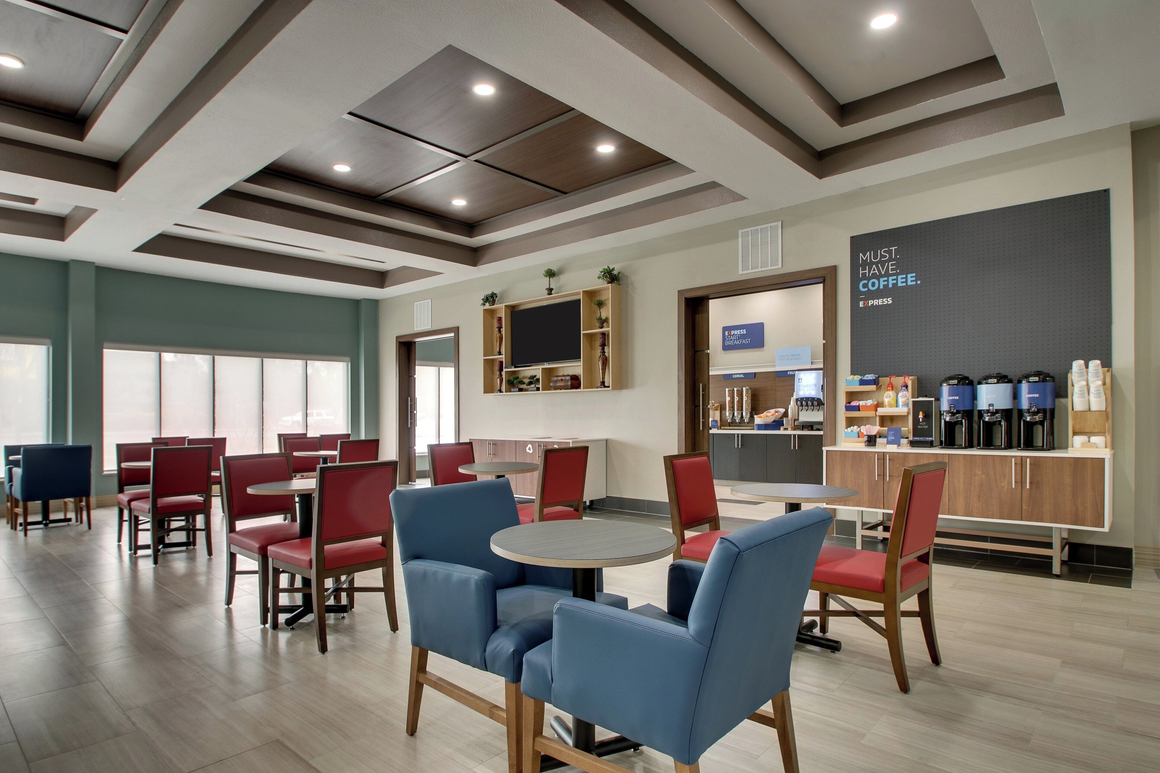 A modern dining area with red and blue chairs, a round table, and a coffee bar with various coffee machines.