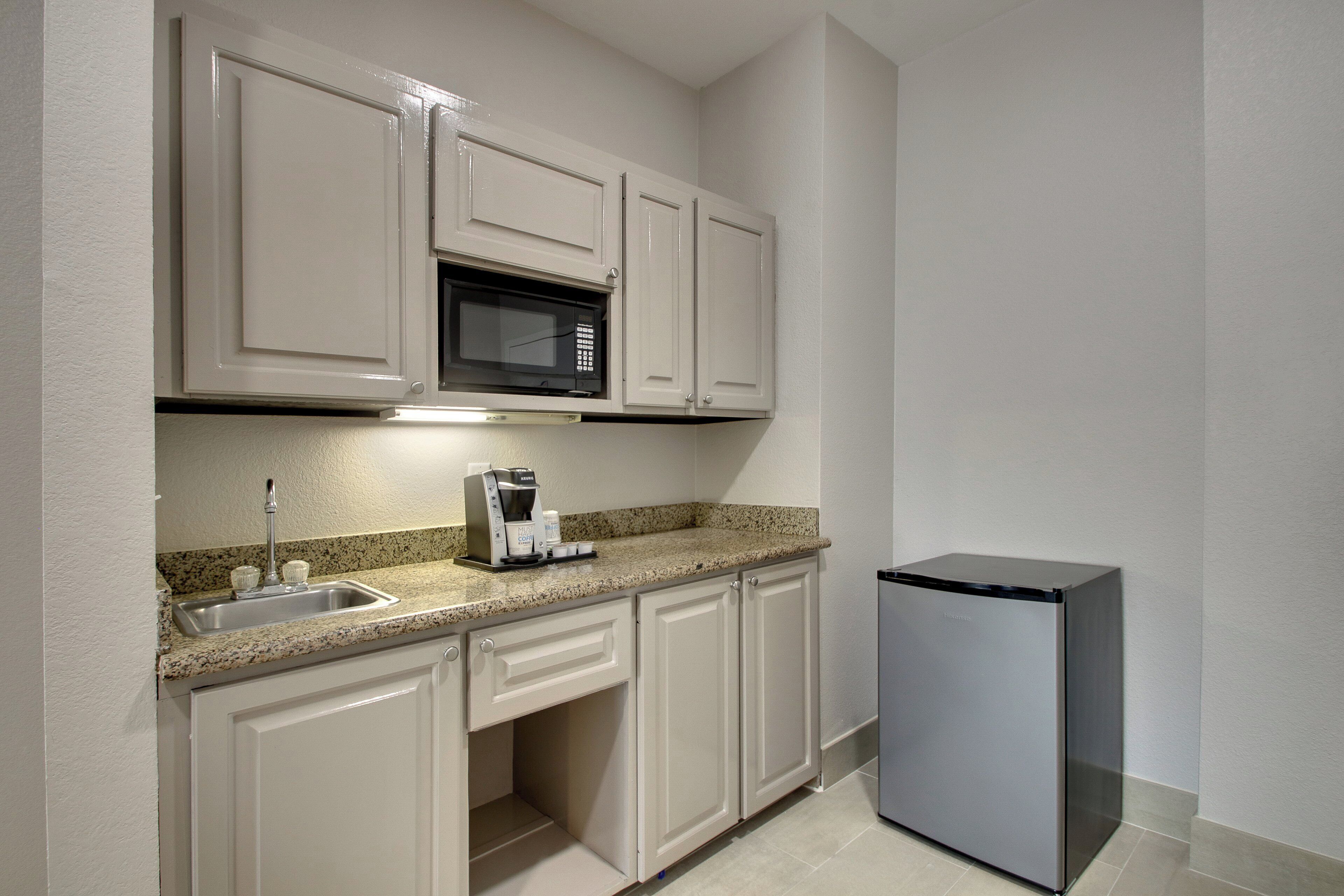 A kitchen with white cabinets, a stainless steel refrigerator, a microwave, and a coffee maker.