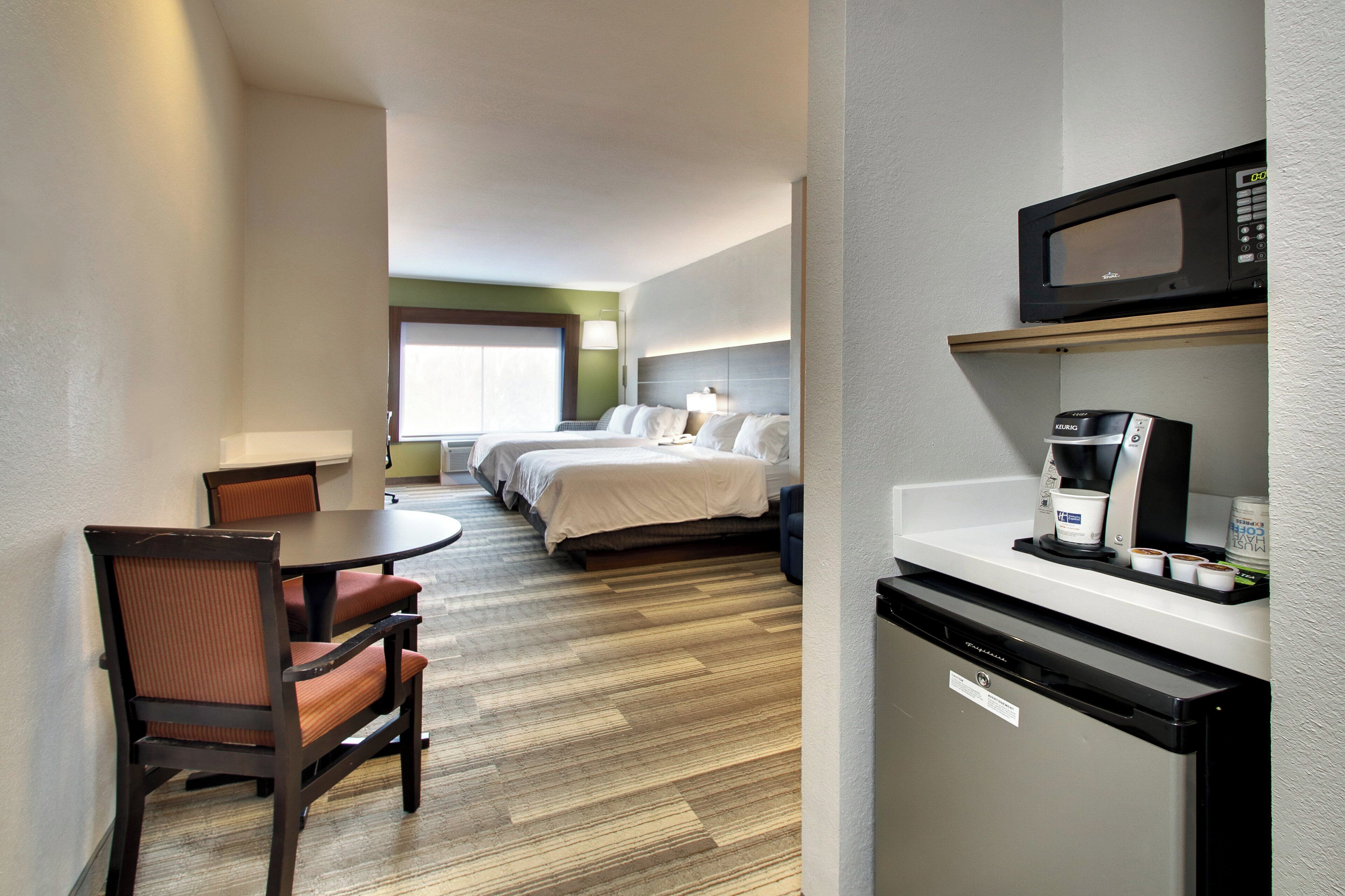 A hotel room with a bed, a dining table with chairs, a microwave, and a coffee maker.