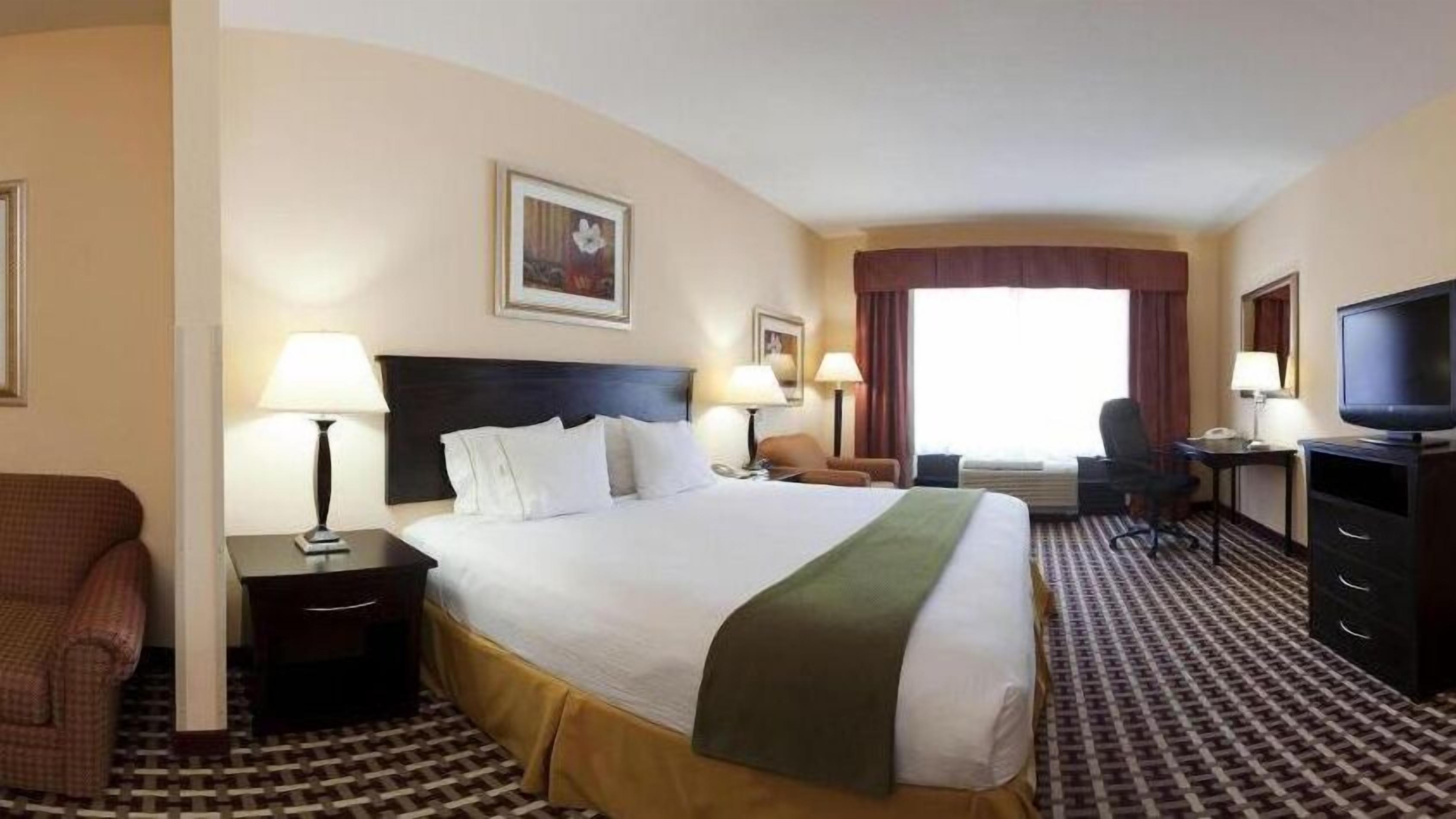 Una habitaci ón de hotel con una cama grande, dos mesitas de noche, un escritorio con silla, una televisión y una ventana con cortinas.